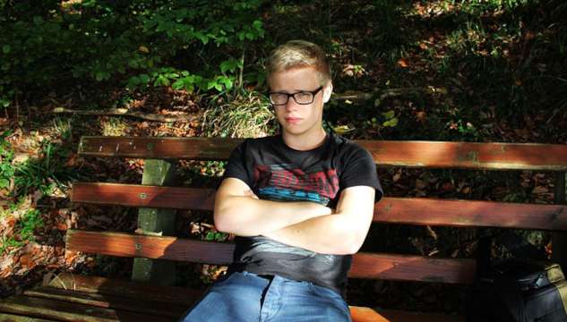 a very frustrated young man sitting on a bench with his arms crossed.